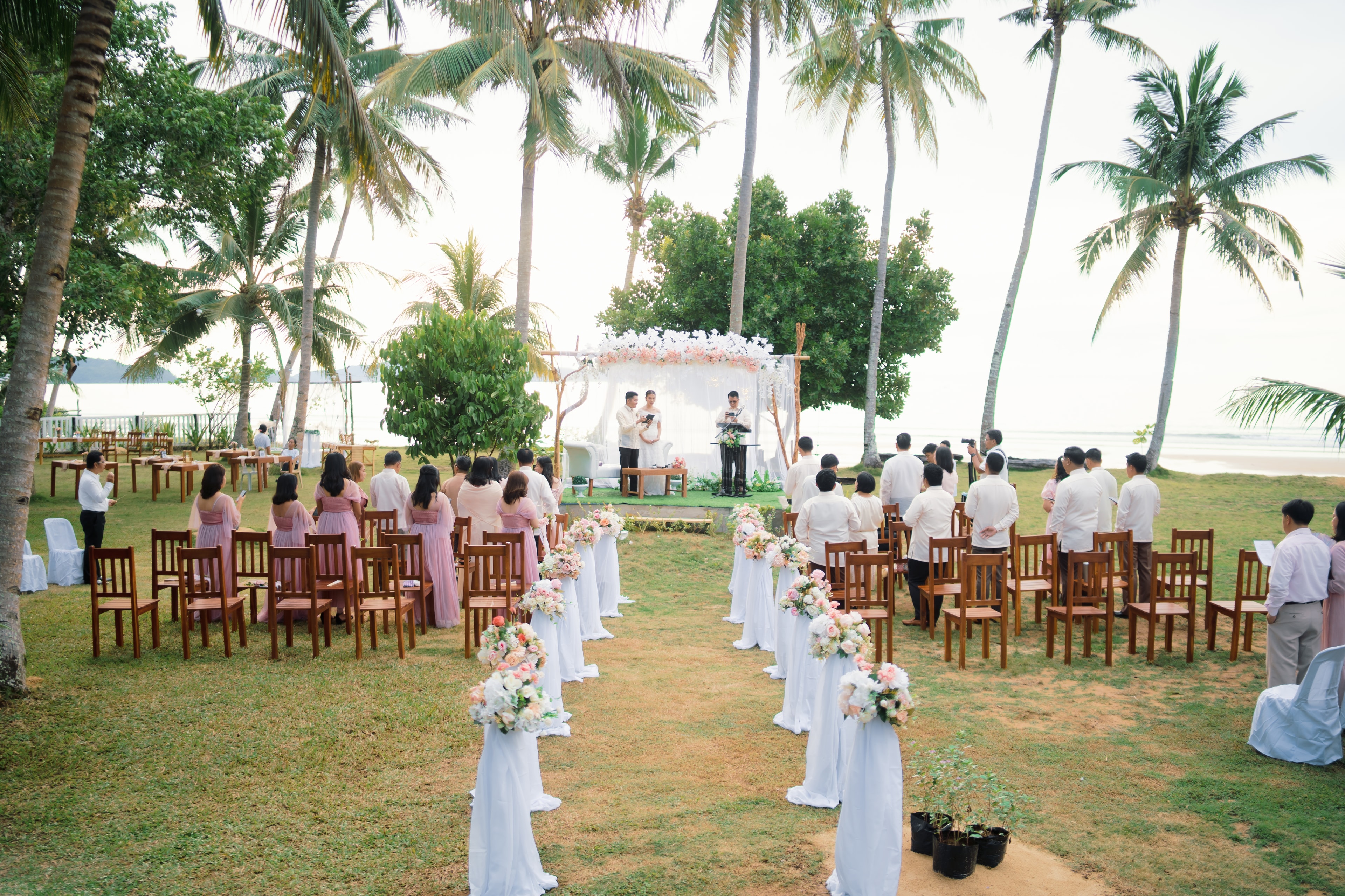 Outdoor wedding ceremony at BAIBAI Beach Resort with palm trees and ocean backdrop